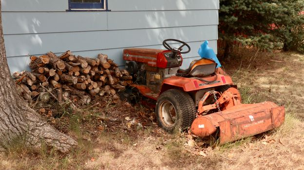 An old red tractor beside a stack of firewood outdoors.